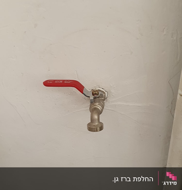ברז עם ידית אדומה על קיר לבן